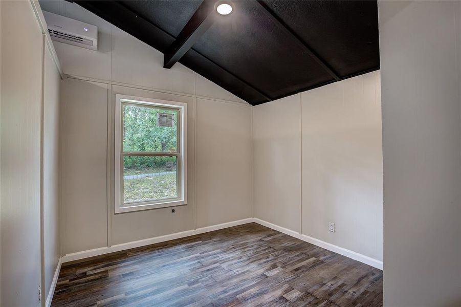 Spare room featuring lofted ceiling with beams, dark wood-type flooring, and a wall unit AC