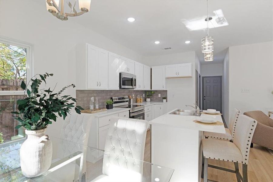 Kitchen featuring stainless steel appliances, light hardwood / wood-style flooring, backsplash, pendant lighting, and white cabinets