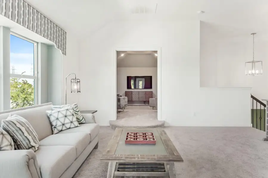 Upstairs living area with vaulted ceiling, gray carpet, sofa, and open doorway to bonus room beyond