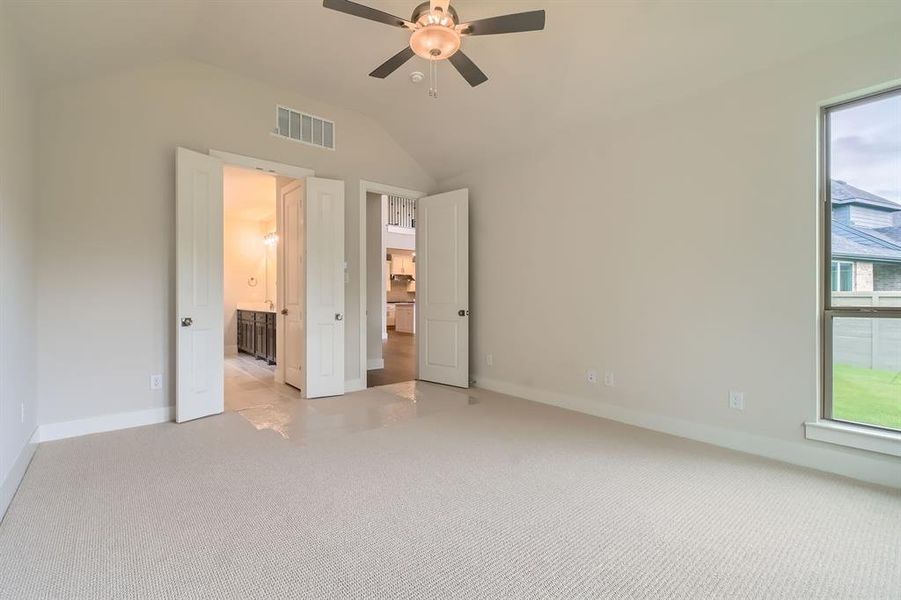Unfurnished bedroom featuring light colored carpet, vaulted ceiling, ensuite bathroom, and ceiling fan Unfurnished bedroom featuring light colored carpet, vaulted ceiling, ensuite bathroom, and ceiling fan