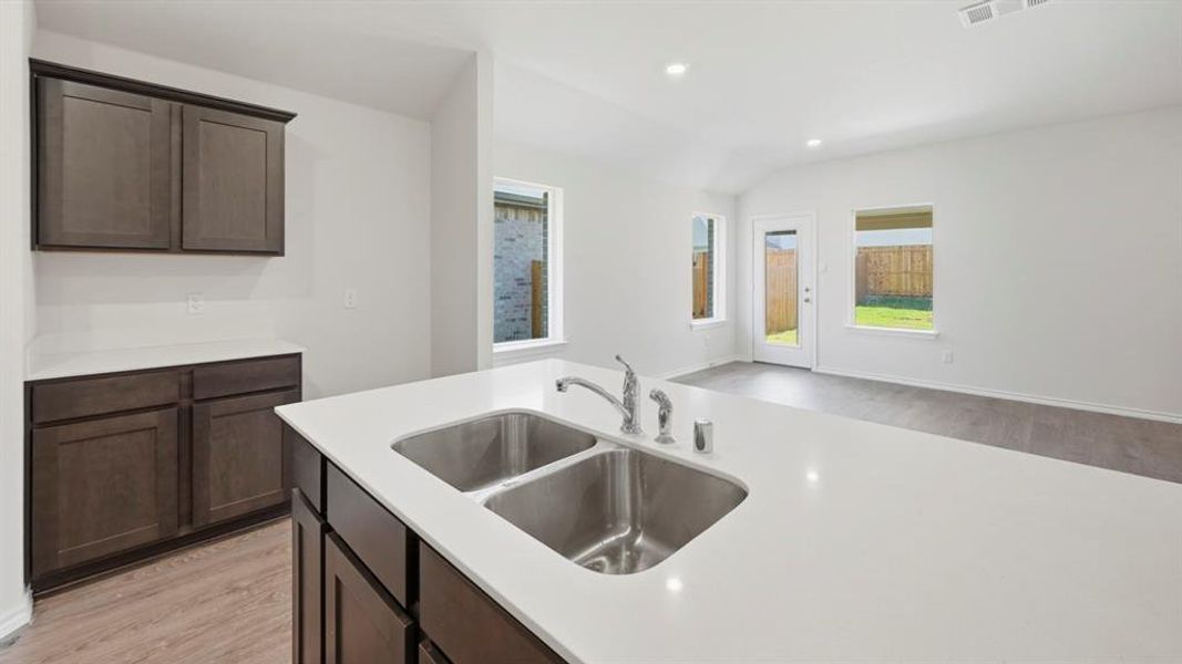 Kitchen featuring light wood-type flooring, dark brown cabinetry, recessed lighting, vaulted ceiling, and light stone counters Kitchen featuring light wood-type flooring, dark brown cabinetry, recessed lighting, vaulted ceiling, and light stone counters