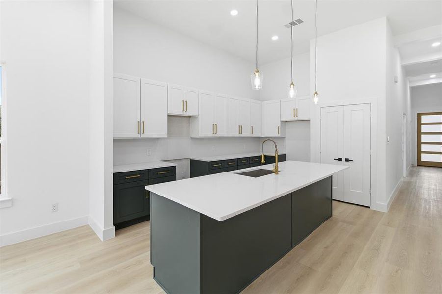 Kitchen with a high ceiling, white cabinetry, pendant lighting, a center island with sink, and light wood-style floors