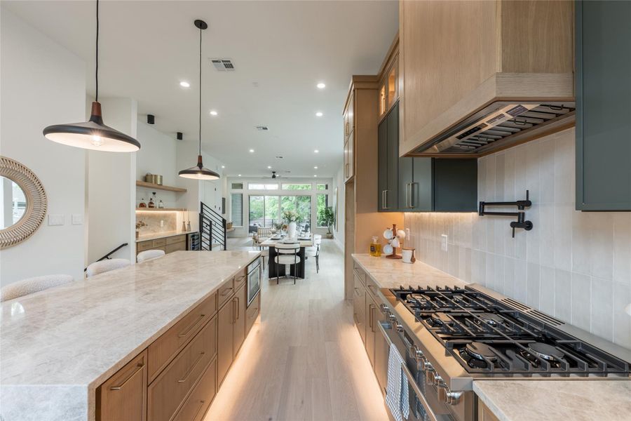 The cook's view. From this side of the island, the range, pot filler, and custom hood form a working line with a full read out to the living area and balcony beyond. The best kitchens don't isolate the host.