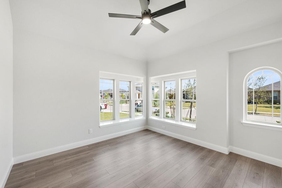 Empty room with hardwood floors, ceiling fan, and large corner windows with neighborhood views Empty room with hardwood floors, ceiling fan, and large corner windows with neighborhood views