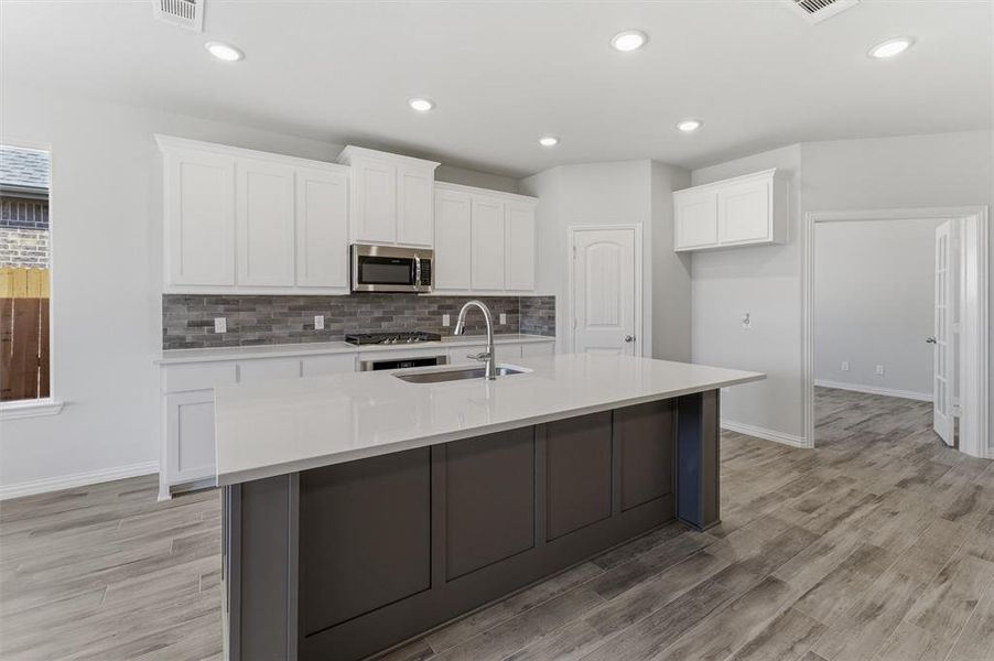 Kitchen with a center island with sink, light wood finished floors, light stone counters, two tone color scheme, and stainless steel microwave