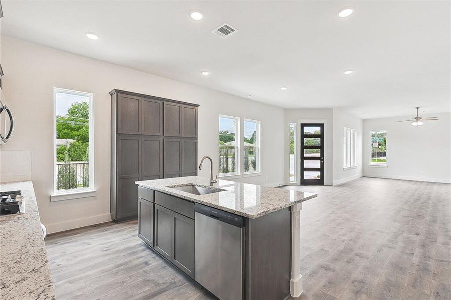 Kitchen featuring dishwasher, sink, light stone counters, dark brown cabinetry, and light hardwood / wood-style floors