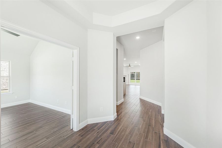 Hallway with dark wood-look floors, white walls, and open view to living area with ceiling fan Hallway with dark wood-look floors, white walls, and open view to living area with ceiling fan