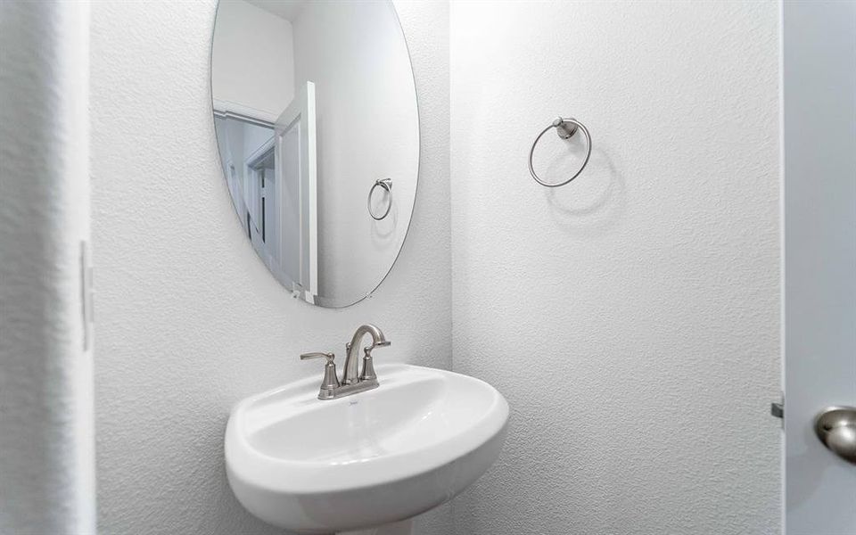 White pedestal sink with brushed nickel faucet, complemented by an oval wall-mounted mirror