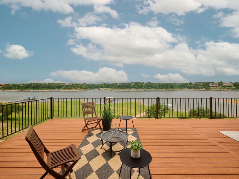 Expansive wood-finish deck with black metal railing overlooking a body of water with distant shoreline and natural landscape