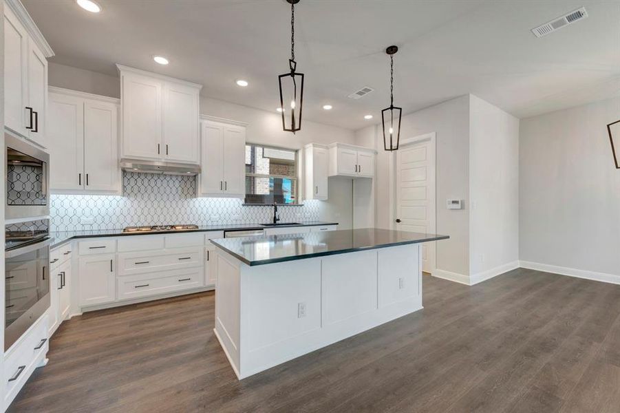 Kitchen with white cabinetry, dark wood-style floors, a center island, and decorative light fixtures