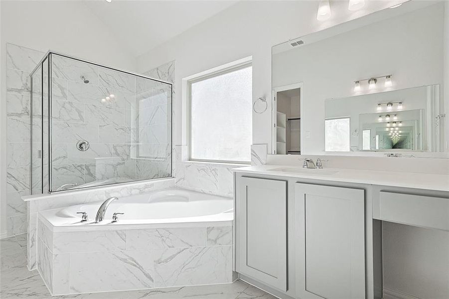 Full bath featuring light marble finish floors, a marble finish shower, vanity, a garden tub, and vaulted ceiling Full bath featuring light marble finish floors, a marble finish shower, vanity, a garden tub, and vaulted ceiling