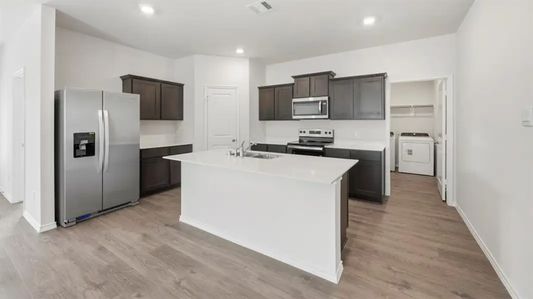 Kitchen featuring appliances with stainless steel finishes, light wood-style floors, a center island with sink, recessed lighting, and dark brown cabinets