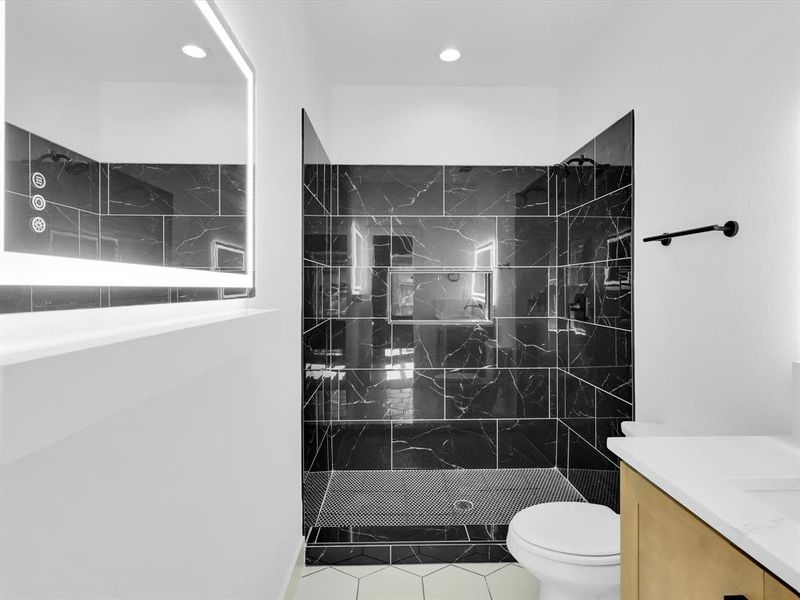 Bathroom with vanity, tiled shower, tile patterned floors, and toilet