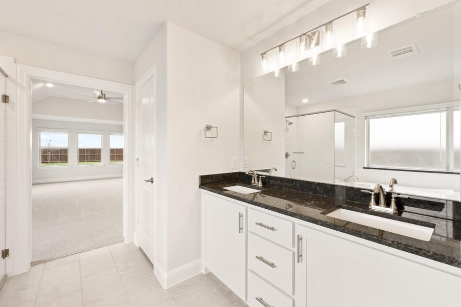 Bathroom with double sink vanity, white cabinets, dark granite countertops, and large mirror with overhead lighting