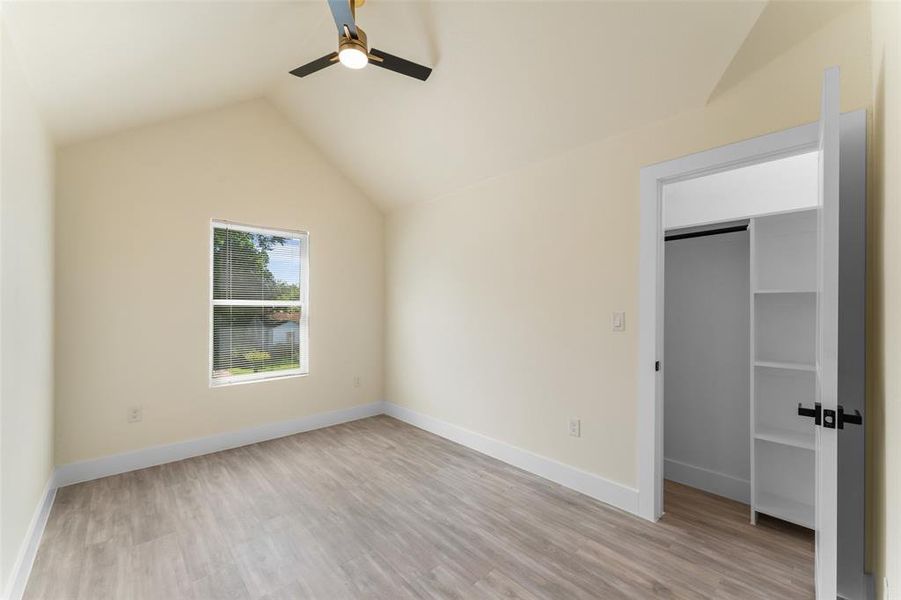 Unfurnished bedroom featuring lofted ceiling, a spacious closet, light wood finished floors, and a ceiling fan