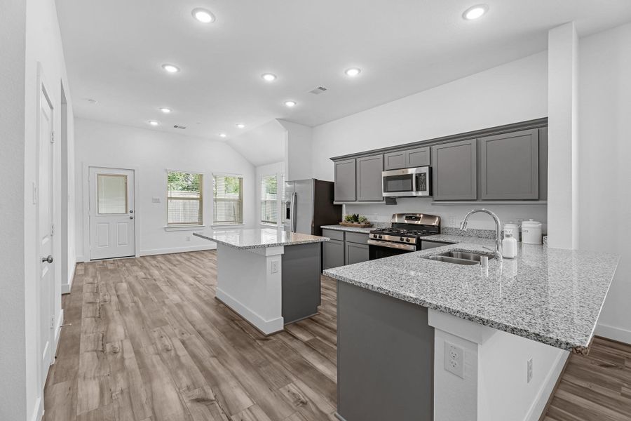 This light and bright kitchen features a large granite island, dark stained cabinets, a large sink overlooking your family room, recessed lighting, and beautiful backsplash.