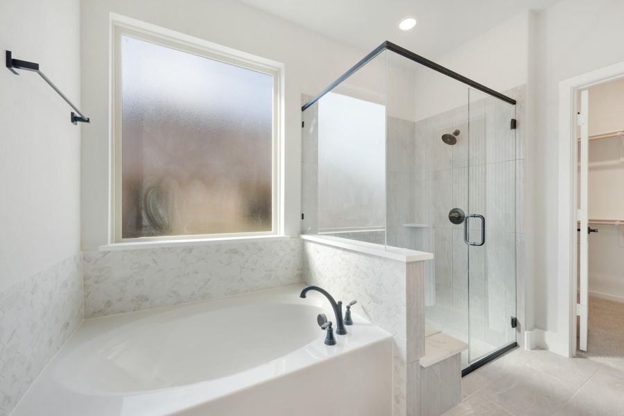 Master bathroom with soaking tub, glass-enclosed shower, marble tile surround, and walk-in closet entry