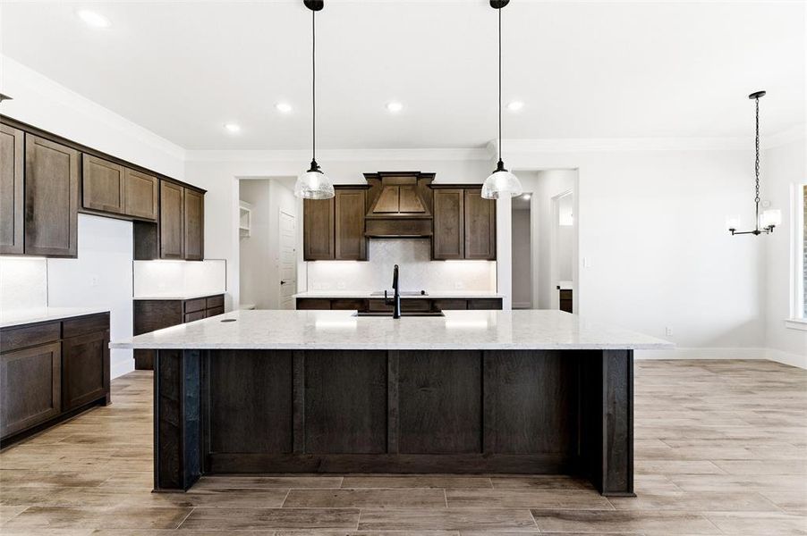 Kitchen with ornamental molding, light stone countertops, hanging light fixtures, and recessed lighting