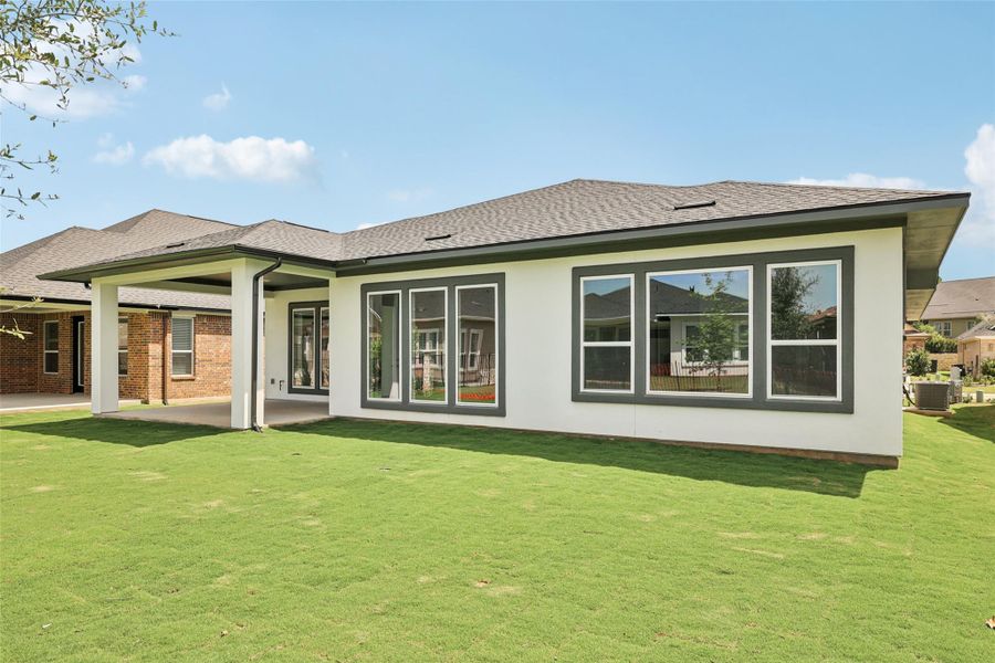 Rear view of house featuring a shingled roof, a lawn, and a patio area