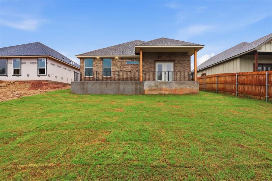 Expansive backyard featuring a manicured lawn, a raised patio with black metal railing, and a covered porch with wood columns Expansive backyard featuring a manicured lawn, a raised patio with black metal railing, and a covered porch with wood columns