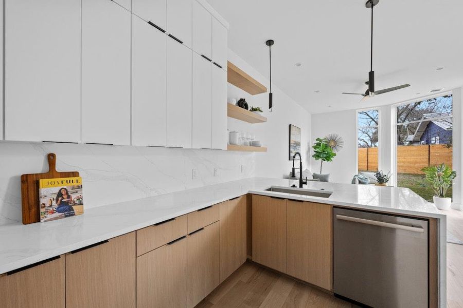 Kitchen featuring light stone counters, modern cabinets, stainless steel dishwasher, open shelves, and light wood-style flooring
