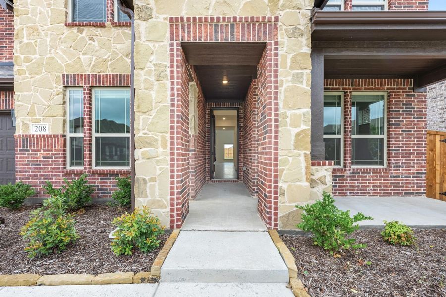 Home entrance with brick and stone archway, concrete walkway, and landscaped mulch beds with shrubs Home entrance with brick and stone archway, concrete walkway, and landscaped mulch beds with shrubs