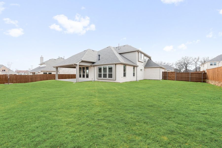 Back of two-story home with large fenced yard, covered patio, and gray shingle roof