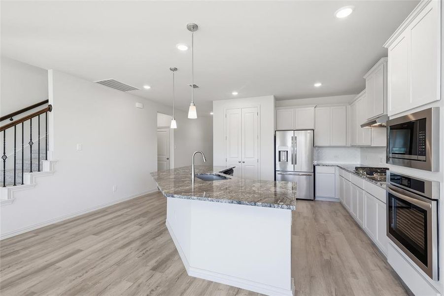 Kitchen featuring stainless steel appliances, a large island, white cabinetry, light wood-style flooring, and light stone countertops Kitchen featuring stainless steel appliances, a large island, white cabinetry, light wood-style flooring, and light stone countertops