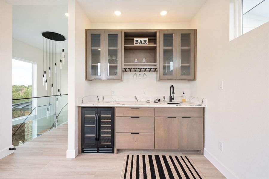Bar area with glass insert cabinets, wine cooler, light stone countertops, light wood-style floors, and recessed lighting