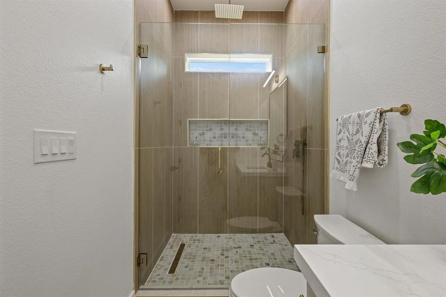 Bathroom featuring a shower with door and toilet