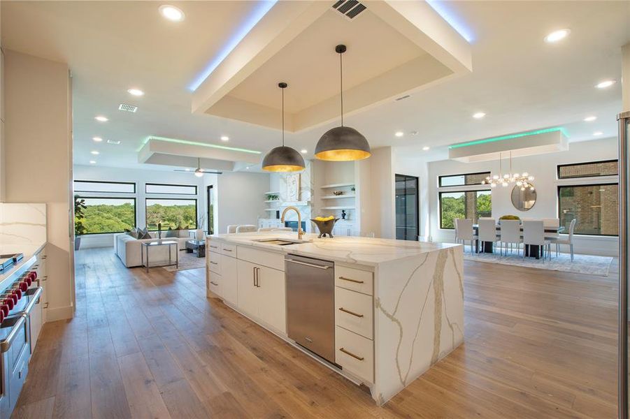 Kitchen with sink, light stone counters, a kitchen island with sink, dishwasher, and a raised ceiling