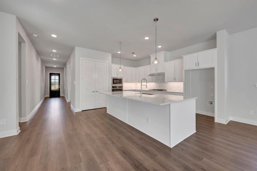 Kitchen featuring white cabinets, a center island with sink, decorative light fixtures, light stone counters, and dark wood-style floors