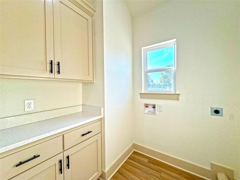 Laundry room featuring light wood-style flooring, a textured wall, hookup for a washing machine, electric dryer hookup, and cabinet space