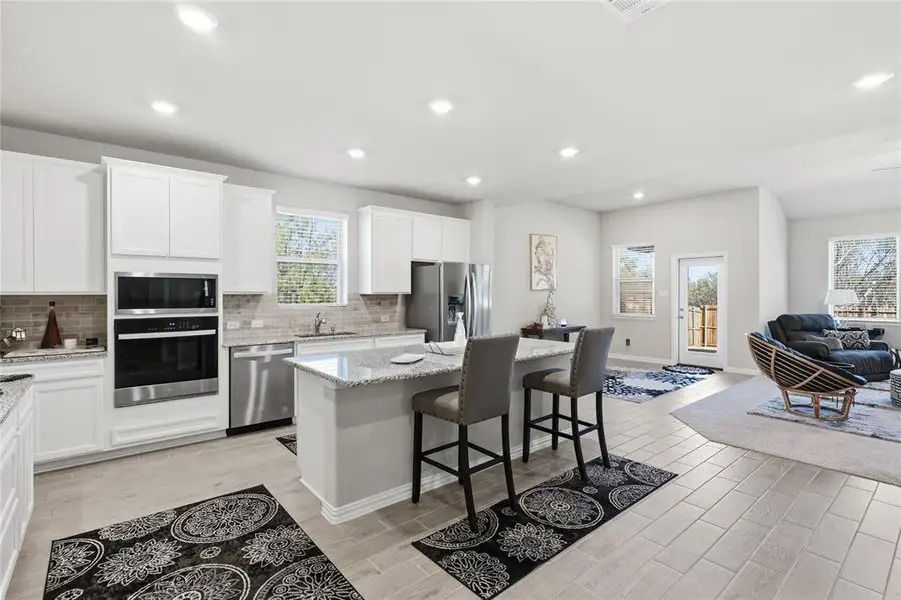 Spacious kitchen featuring white cabinetry, stone-finish countertops, stainless steel appliances, and a central island with seating