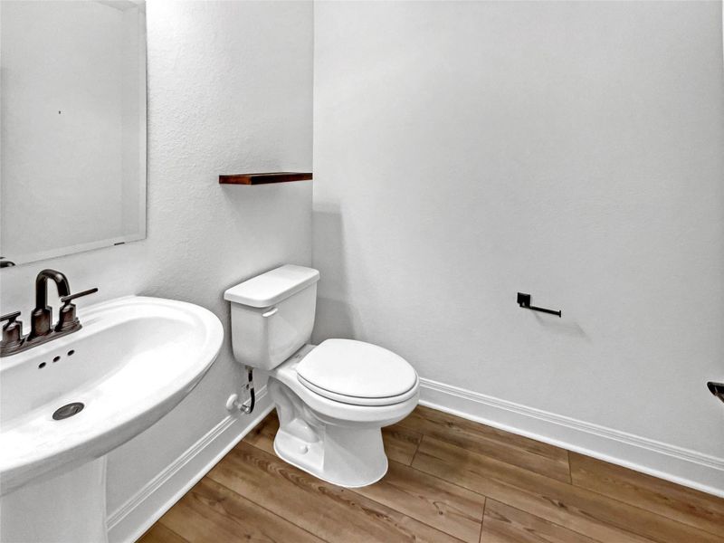 Half bathroom featuring a sink, baseboards, toilet, and wood finished floors