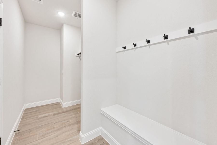 Mudroom with white built-in bench, black wall hooks, and light wood-look flooring