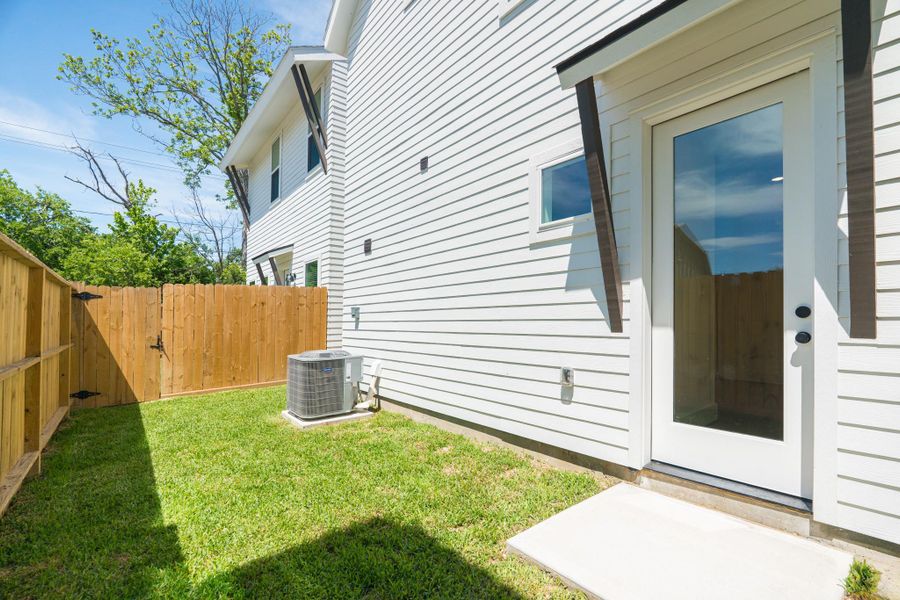 This photo showcases a small, fenced backyard with a grassy area adjacent to a white house exterior. There's a glass door leading inside and an air conditioning unit on a concrete pad. The space is private and well-maintained, ideal for outdoor relaxation.Photo Disclaimer: Photos are representative of the community and may depict a similar floor plan, model home, or previously completed residence. This photo showcases a small, fenced backyard with a grassy area adjacent to a white house exterior. There's a glass door leading inside and an air conditioning unit on a concrete pad. The space is private and well-maintained, ideal for outdoor relaxation.Photo Disclaimer: Photos are representative of the community and may depict a similar floor plan, model home, or previously completed residence.