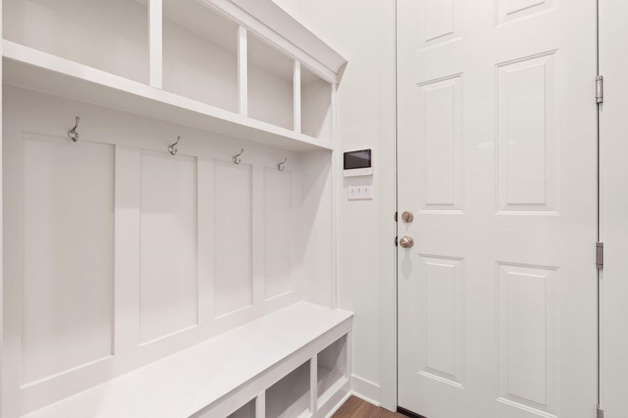 Built-in white storage bench with open cubbies, coat hooks, and overhead shelving, complemented by a paneled entry door Built-in white storage bench with open cubbies, coat hooks, and overhead shelving, complemented by a paneled entry door
