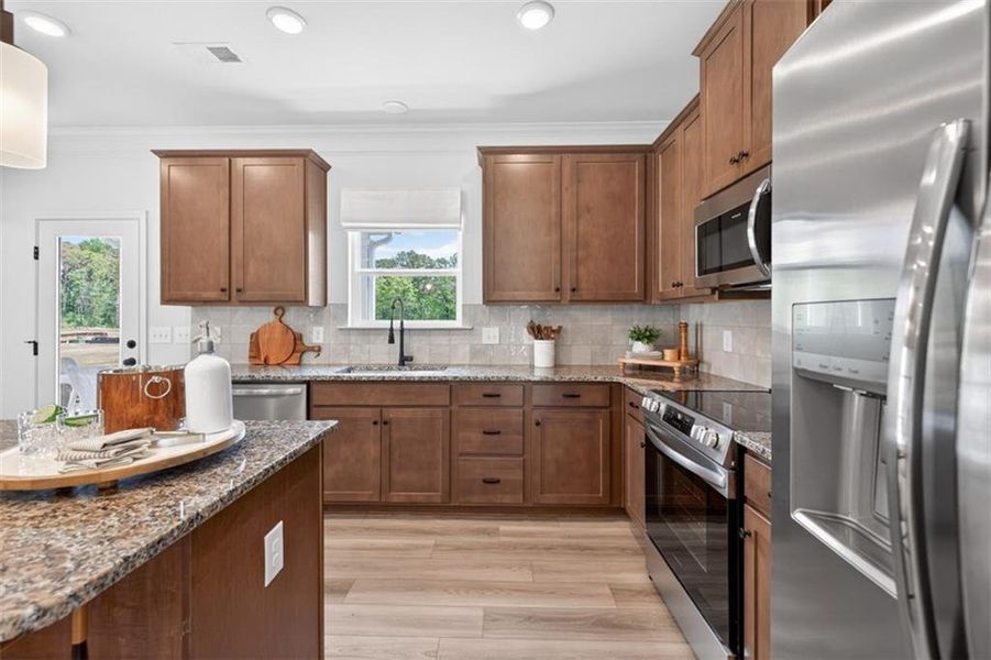 Modern kitchen featuring wood-finish cabinetry, speckled countertops, stainless steel appliances, and wood-finish flooring