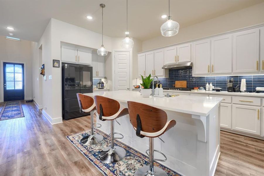 Kitchen featuring white cabinetry, black fridge, and a center island with sink