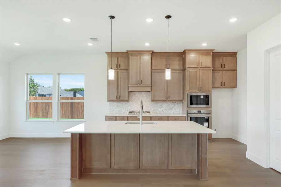 Kitchen with large center island, wood cabinets, herringbone tile backsplash, and stainless steel appliances