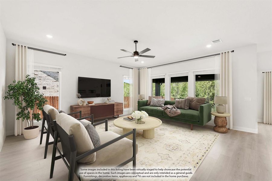 Bright living room with light wood floors, ceiling fan, green sofa, and large windows with backyard views Bright living room with light wood floors, ceiling fan, green sofa, and large windows with backyard views