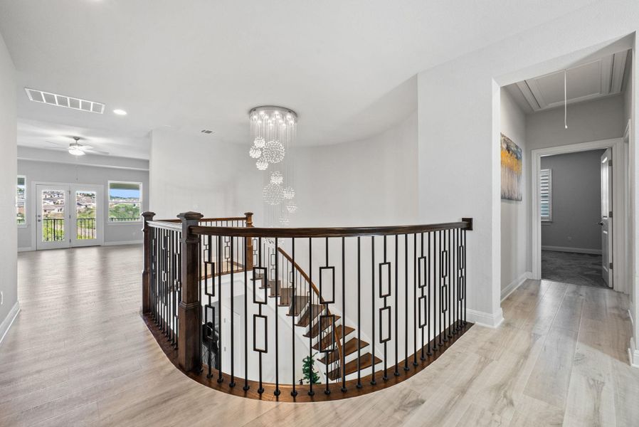 Hall with light wood-style floors, suspended lighting, and an upstairs landing