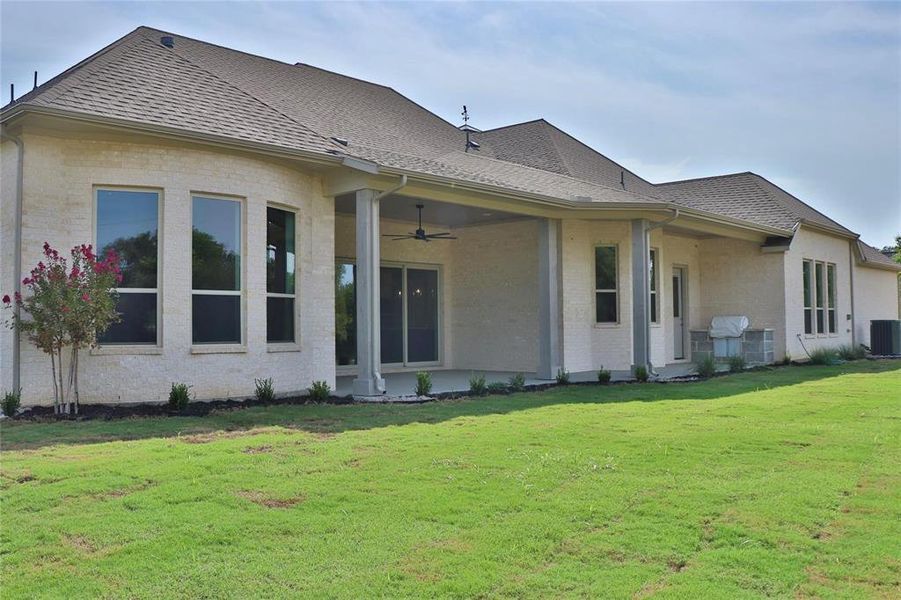 Back of property with brick siding, a ceiling fan, a yard, roof with shingles, and cooling unit
