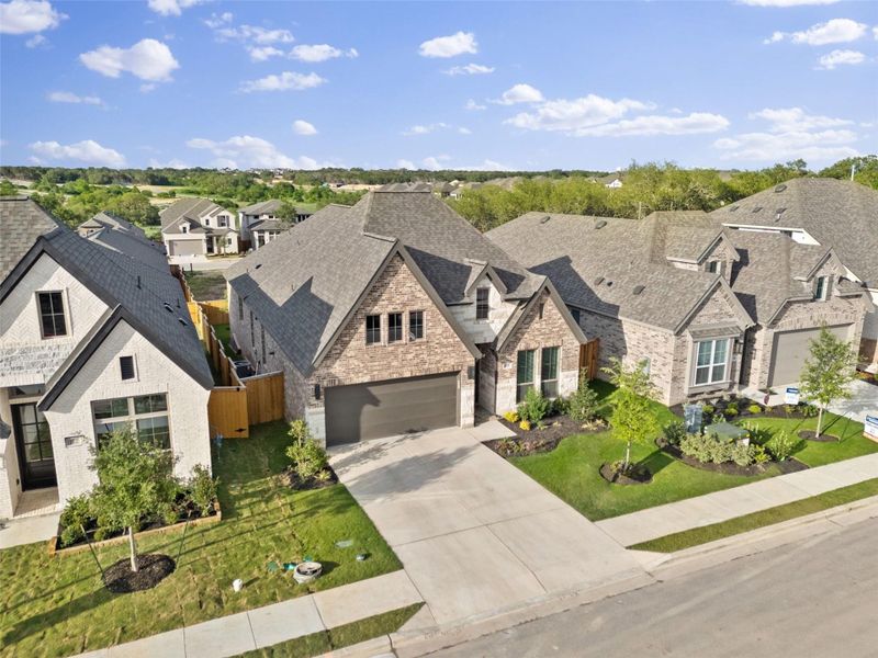 Exterior featuring a brick facade with stone accents, a multi-gabled roofline, an attached two-car garage, a concrete driveway, and a landscaped front yard with planted trees and shrubs