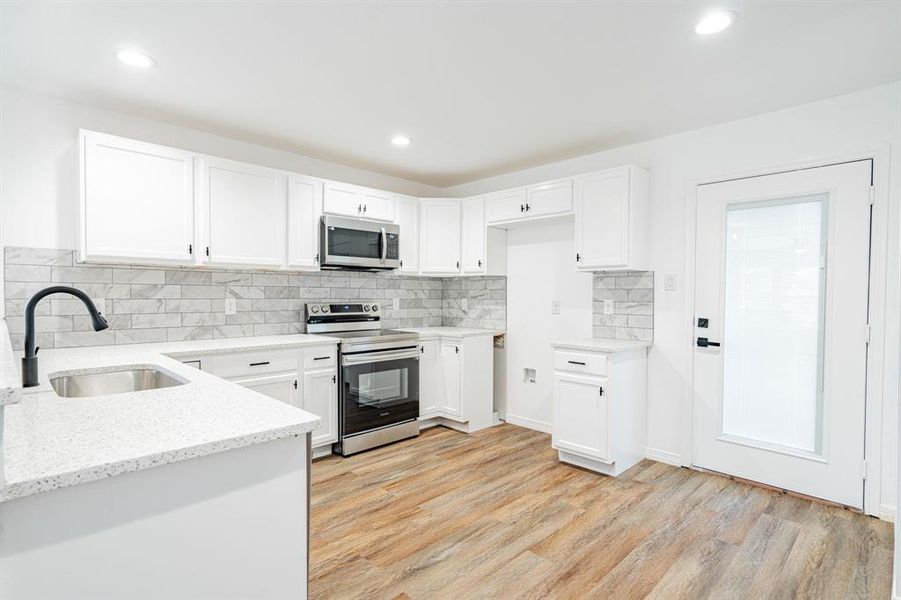 Kitchen with appliances with stainless steel finishes, light hardwood / wood-style flooring, white cabinets, and sink