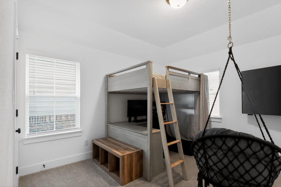 Carpeted room featuring two windows with blinds, a ceiling-mounted light fixture, and a built-in bunk bed structure with an integrated desk Carpeted room featuring two windows with blinds, a ceiling-mounted light fixture, and a built-in bunk bed structure with an integrated desk