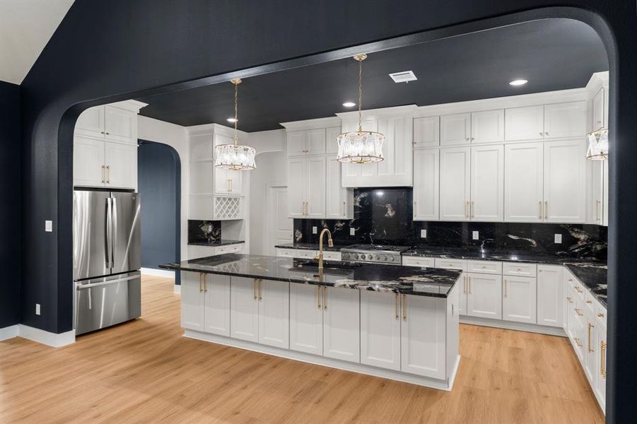 Kitchen with arched walkways, freestanding refrigerator, a center island with sink, backsplash, and dark stone countertops