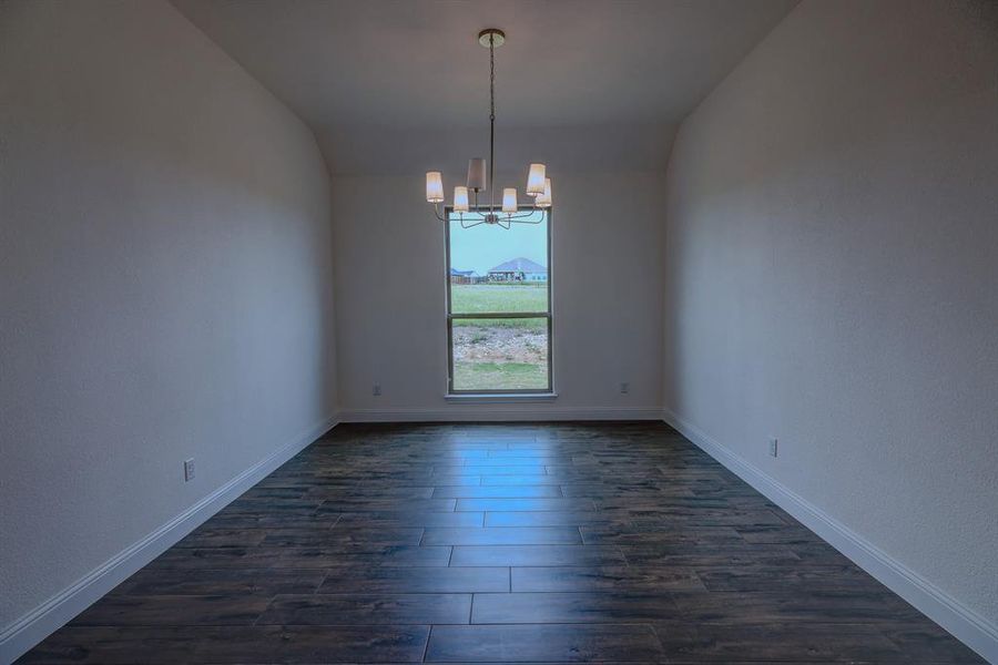 Spare room with a chandelier, dark wood-style flooring, baseboards, and vaulted ceiling