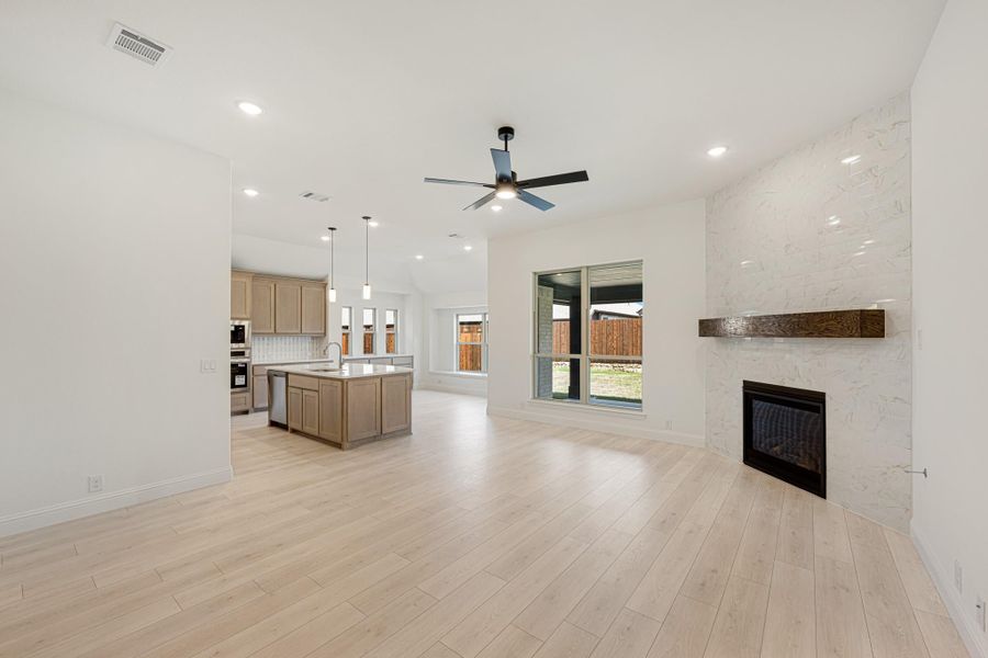 Open living area with light wood floors, marble fireplace, and kitchen with island visible in background